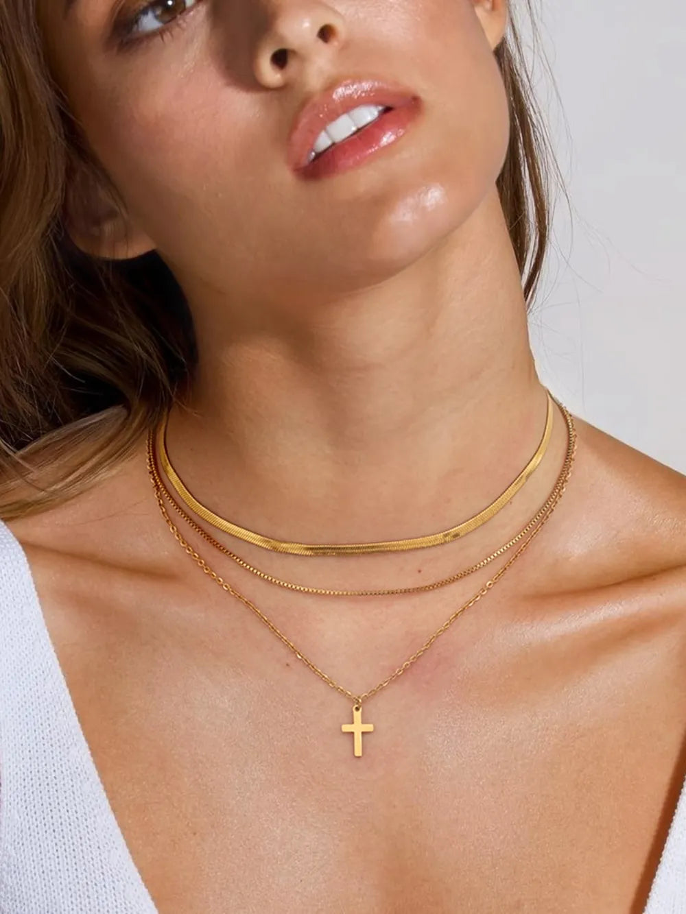 Close-up of a woman wearing a three-layered 18K gold-plated cross necklace with varying chain styles.