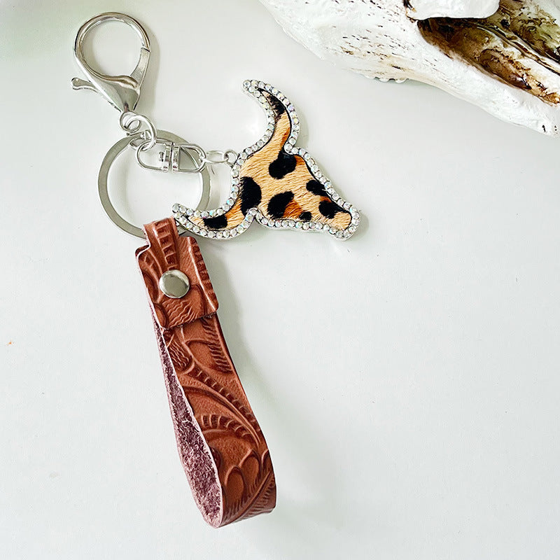Rhinestone bull head keychain with leopard print and embossed brown genuine leather strap attached to metal ring and clasp.