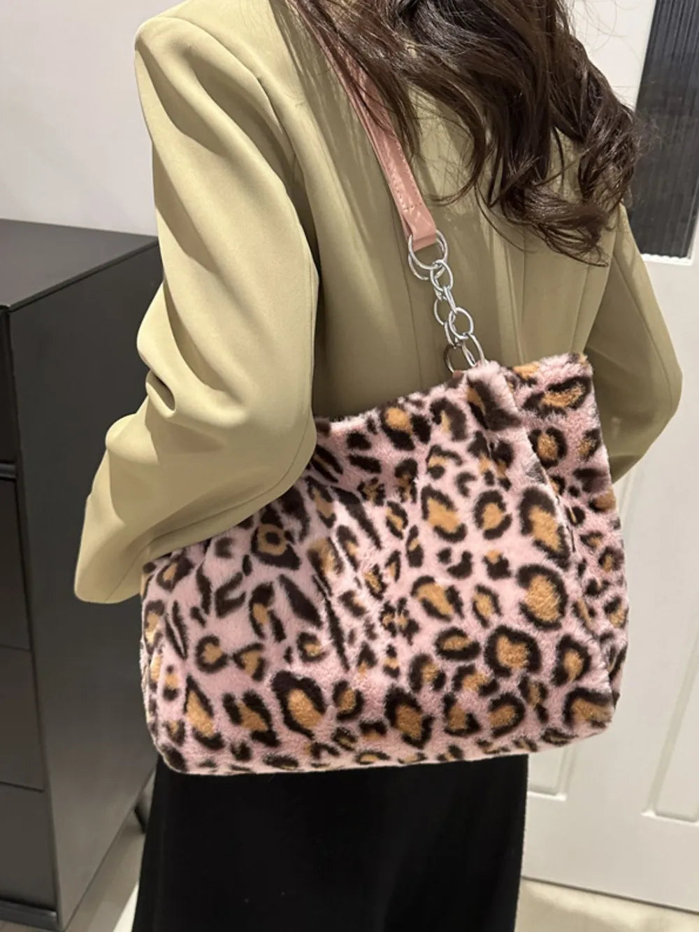 Woman wearing a large leopard print faux fur shoulder bag with pink adjustable strap and chain detail