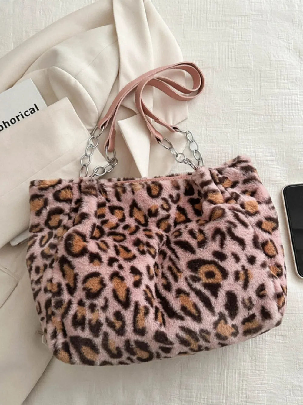 Large leopard print shoulder bag made of soft faux fur with leather straps and chain details on a white fabric background