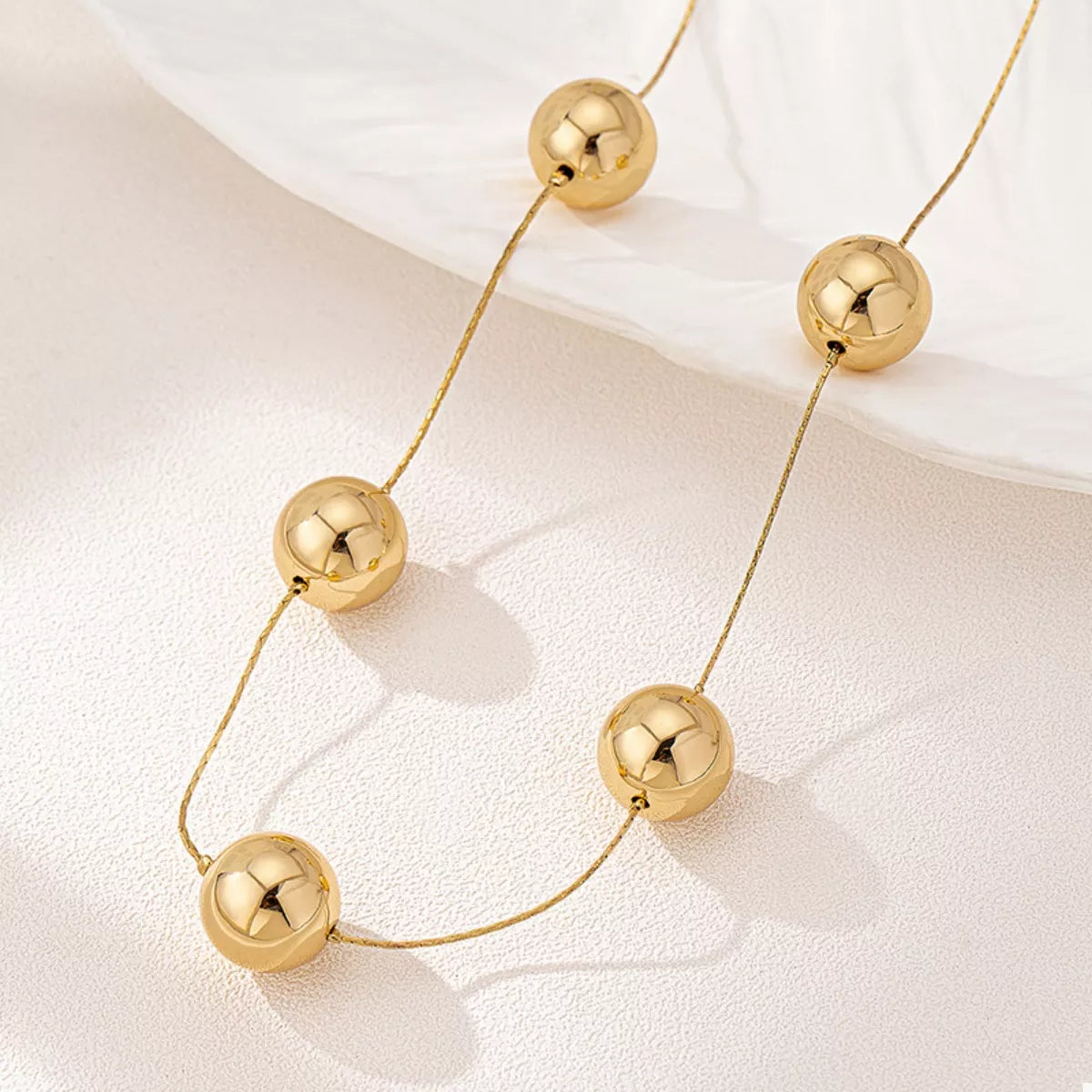 Close-up of a golden sphere statement necklace with five polished 18K gold-plated beads on a delicate chain.