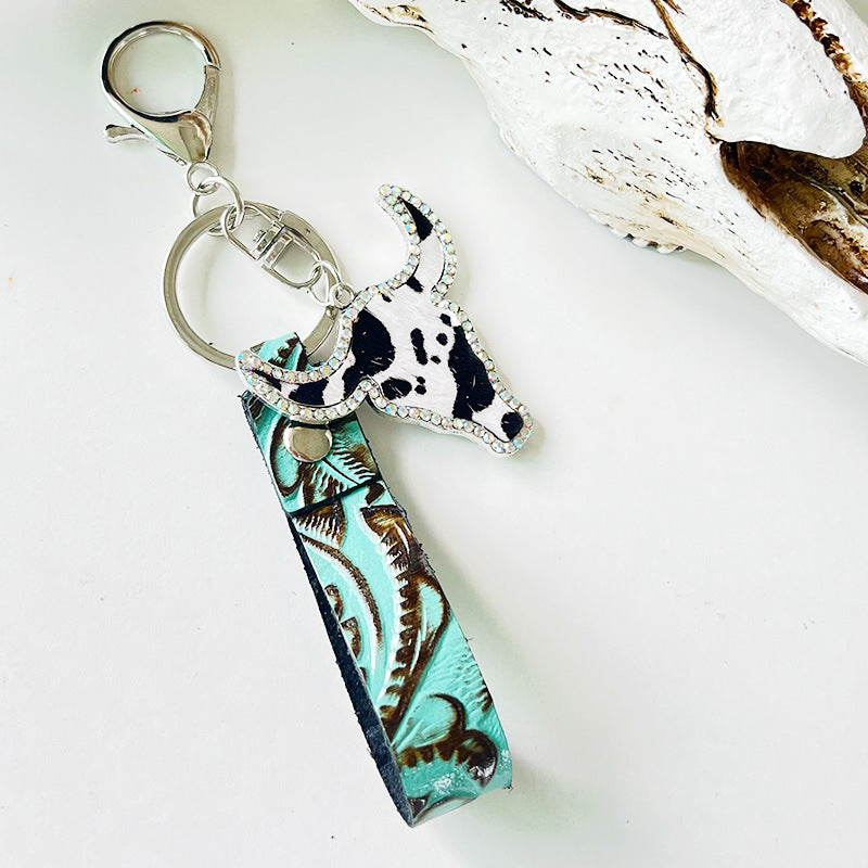 Rhinestone bull head keychain with genuine leather teal patterned strap and silver alloy hardware on white background.