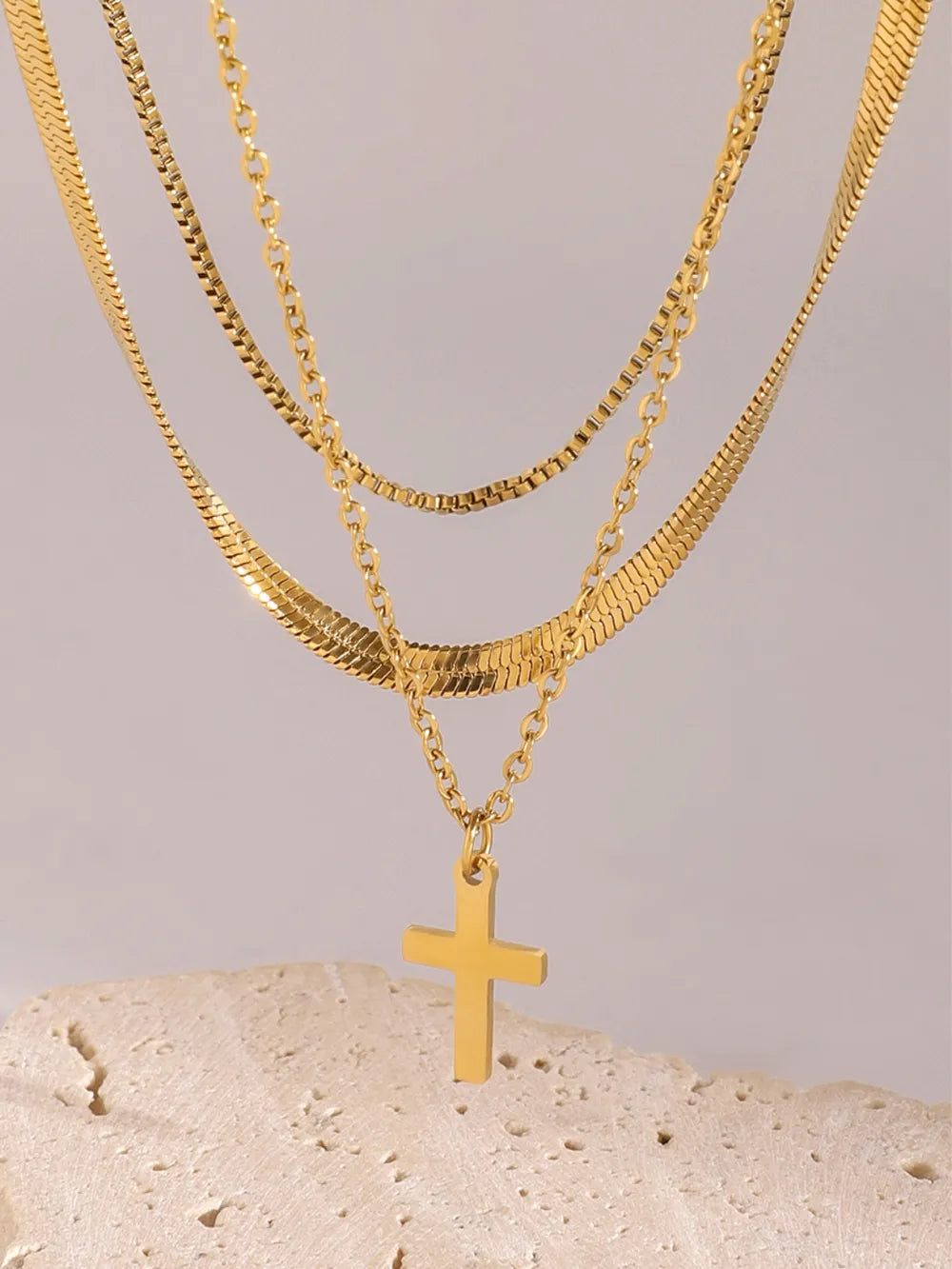Three-layered 18K gold-plated cross necklace with varying chain styles on a neutral background.