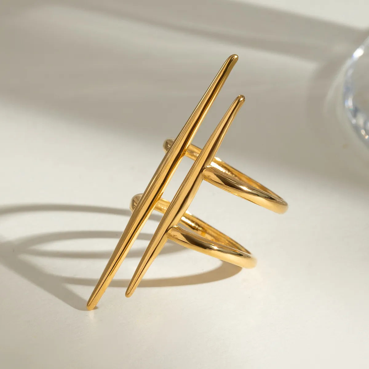 Gold-plated stainless steel asymmetrical ring with sleek modern design casting shadow on light background