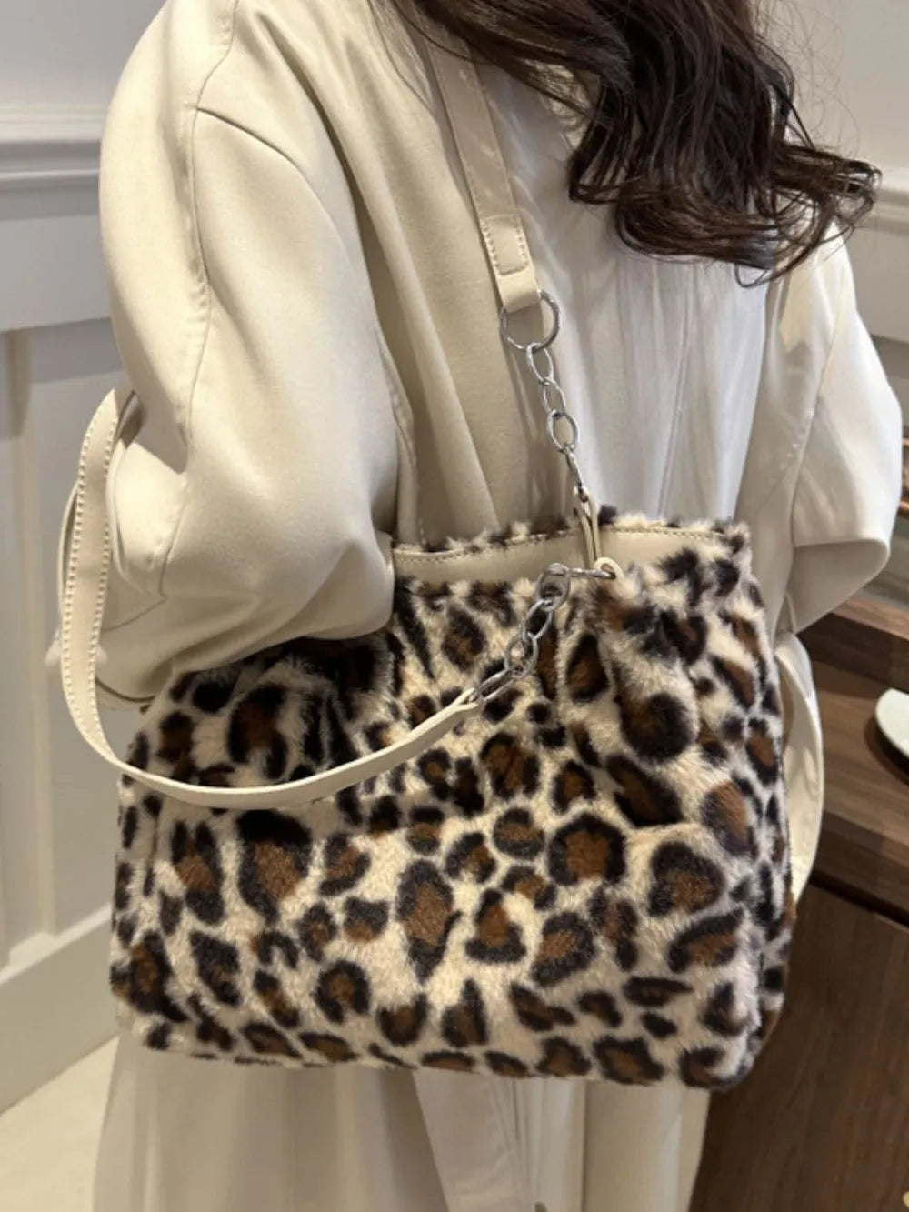 Soft faux fur leopard print shoulder bag with adjustable strap worn over beige coat by a woman