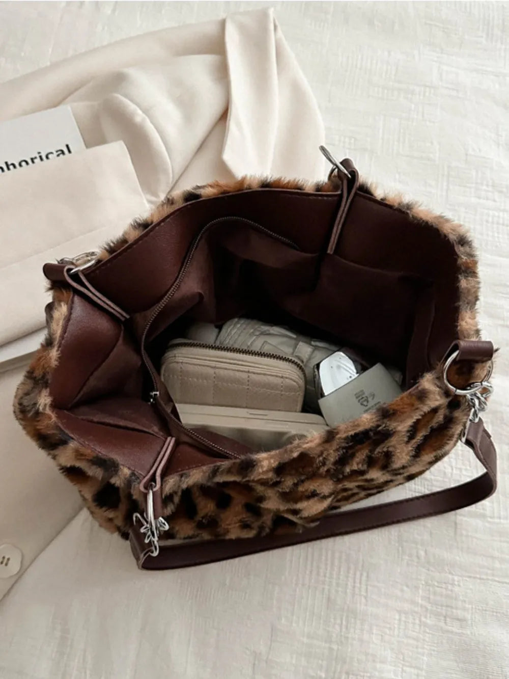 Open leopard print shoulder bag made of soft faux fur showing interior compartments and accessories inside