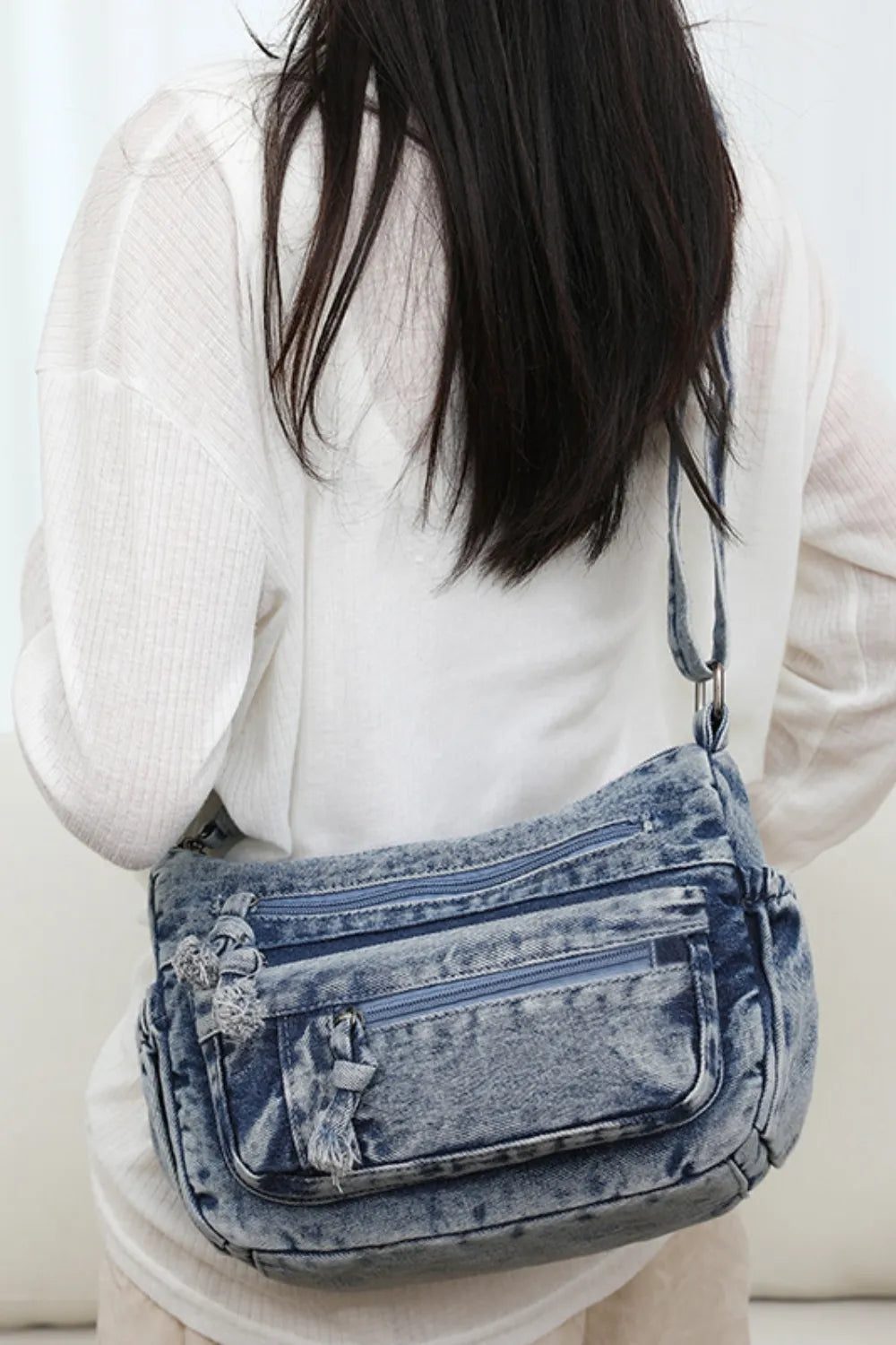 Denim crossbody bag with multiple zippered pockets worn over shoulder, medium size for everyday use.