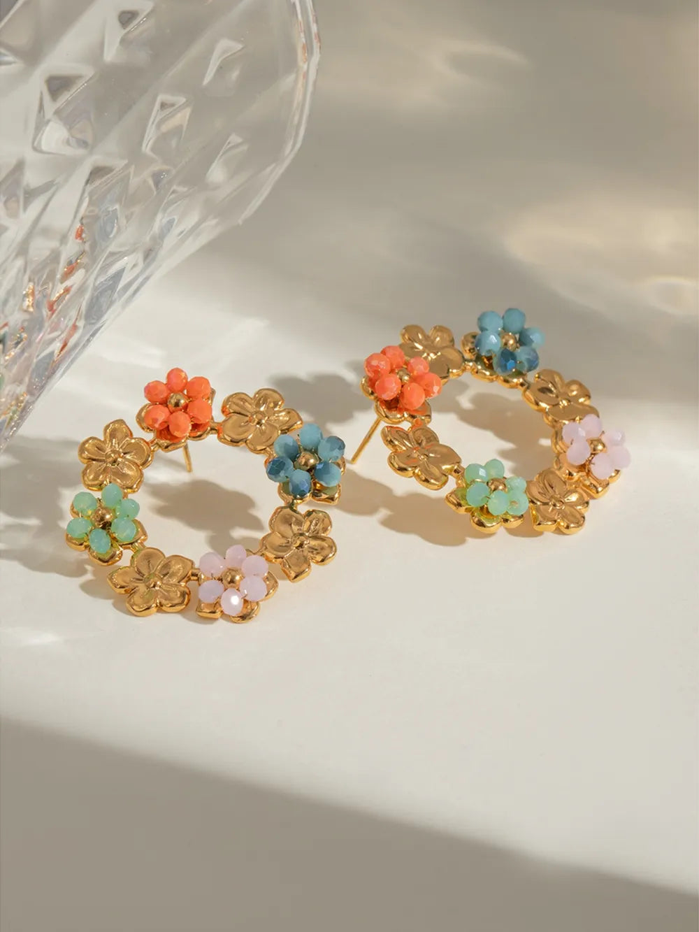 Gold plated stainless steel flower earrings with multicolored synthetic crystals in a circular design on a light background