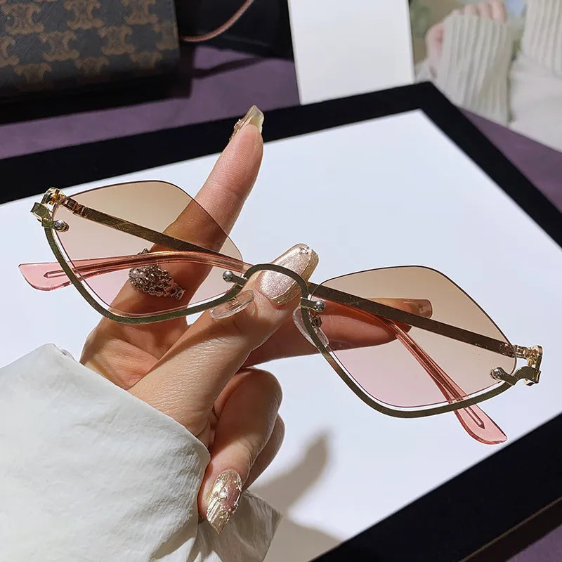 Hand holding metal frame cat eye sunglasses with pink tinted UV400 polycarbonate lenses on white surface