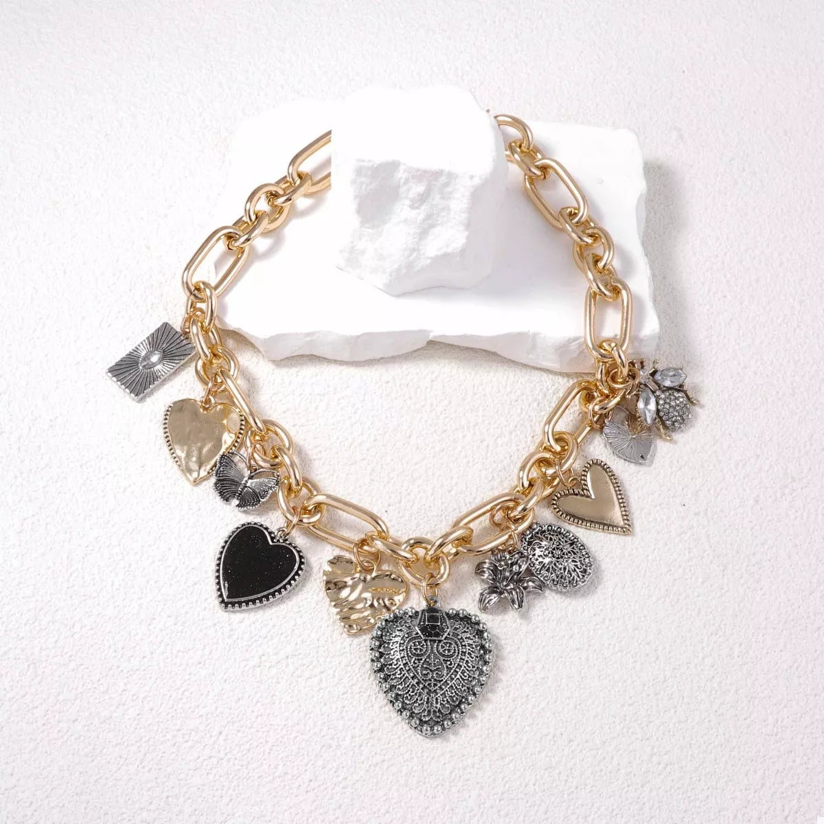 Vintage-inspired gold-plated charm necklace with heart and nature-themed pendants on a thick chain.