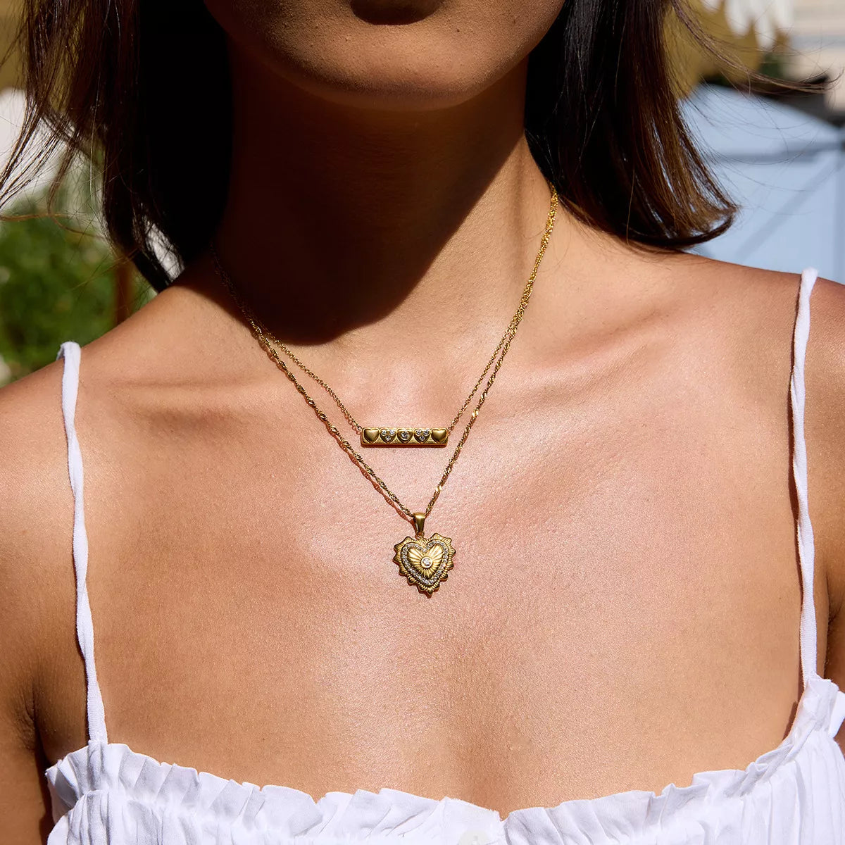 Woman wearing an 18K gold-plated heart-shaped zircon pendant necklace with layered delicate chains and white top