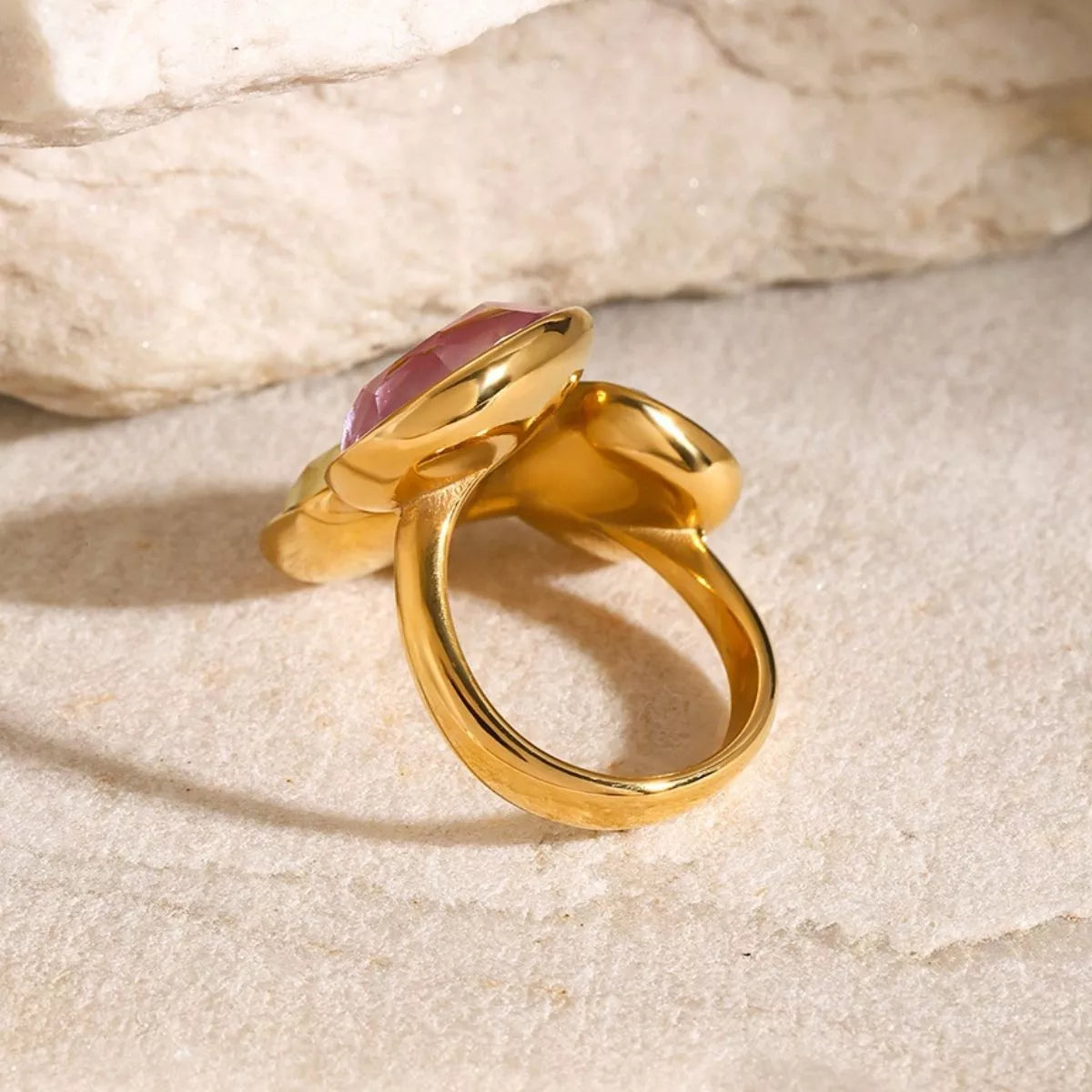 18k gold plated adjustable ring with pink gemstone and rhinestone in an elegant bypass design on stone surface