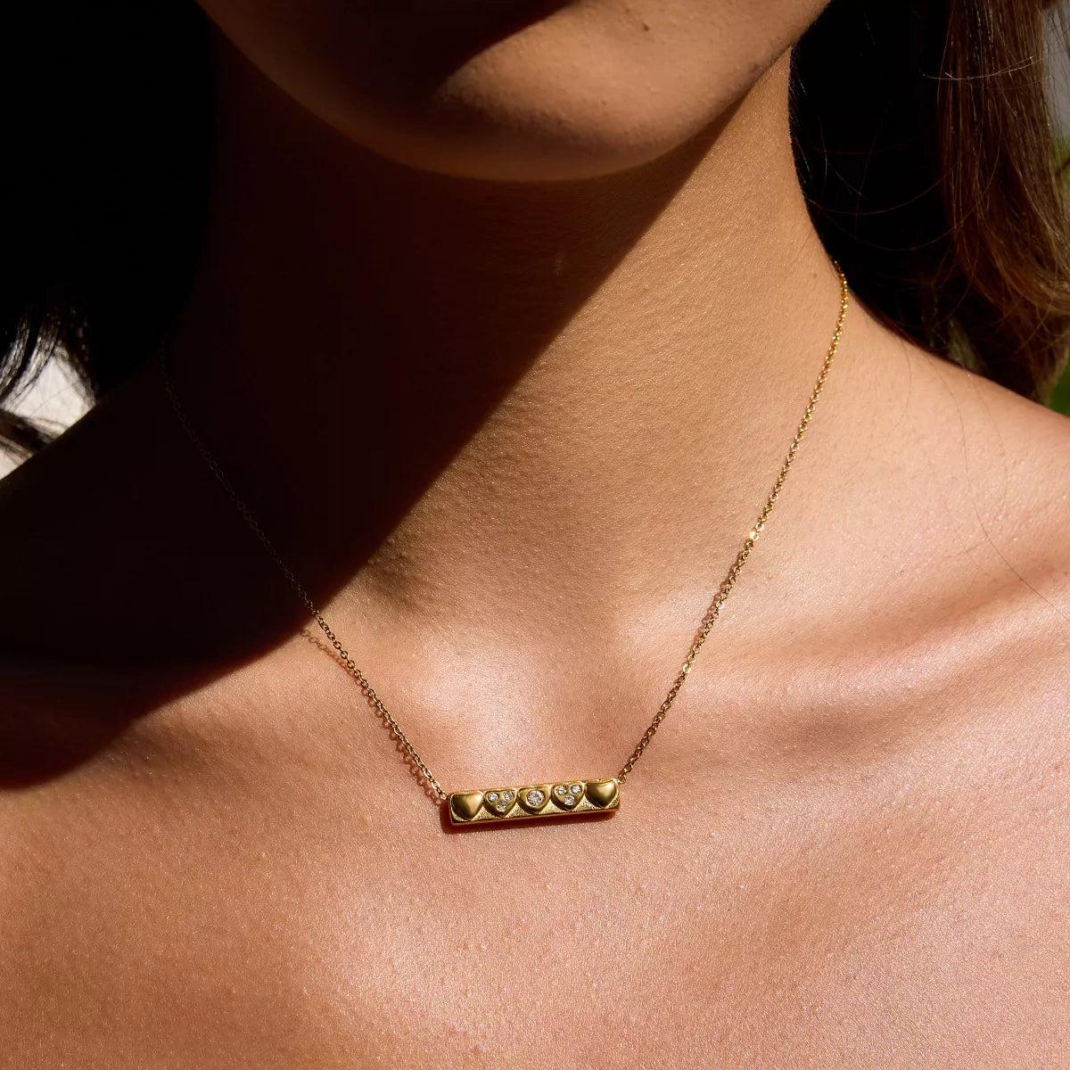 Close-up of a woman wearing an 18K gold-plated heart pendant necklace with zircon accents on a delicate chain