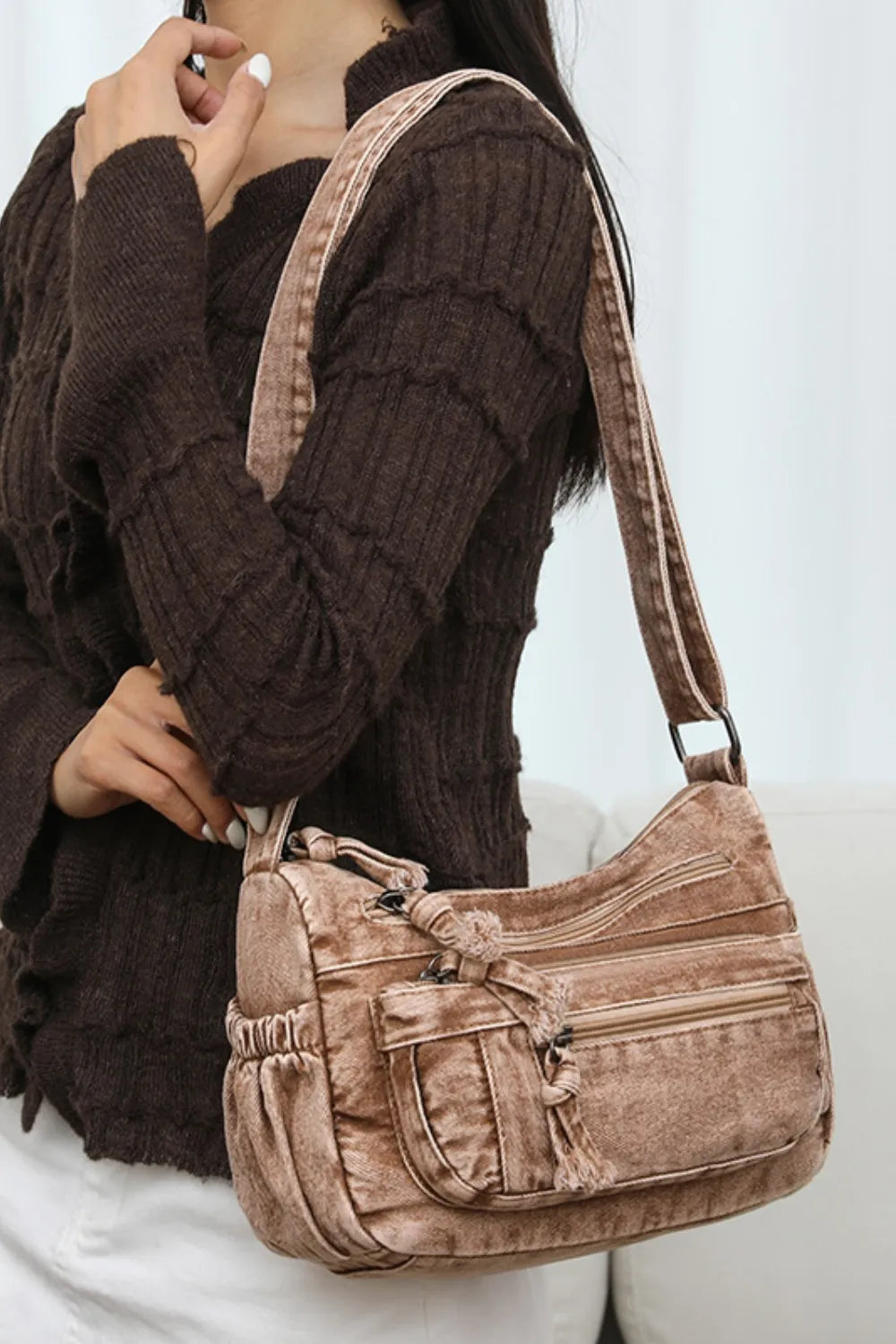 Woman wearing a soft brown velvet crossbody bag with multiple zippered compartments over a dark sweater