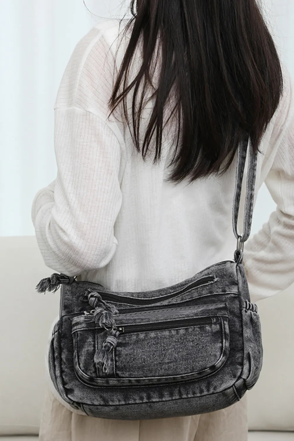 Woman wearing a medium-sized durable gray denim crossbody bag with multiple zippered compartments and adjustable strap