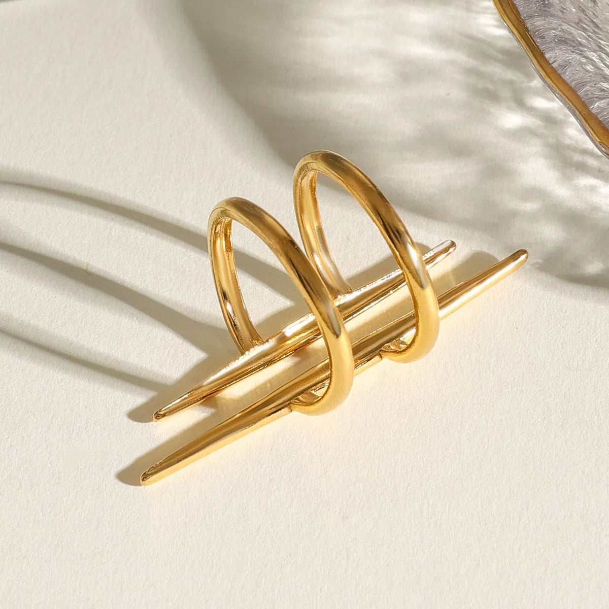 Gold-plated stainless steel asymmetrical ring with modern, sleek design casting shadows on a light surface