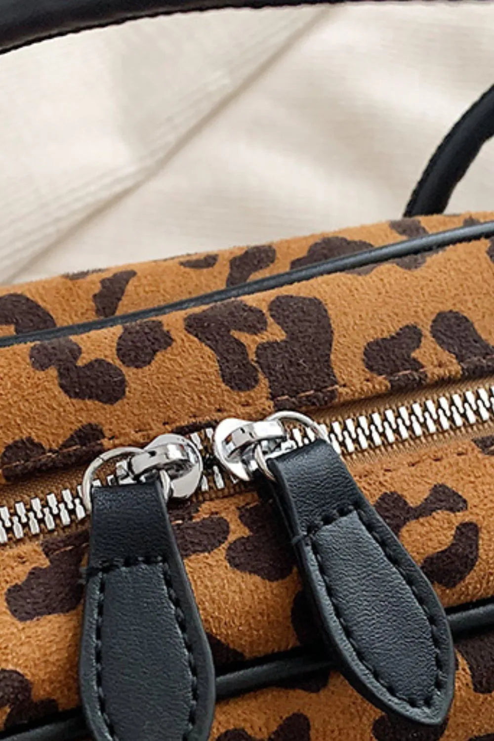 Close-up of leopard print suede shoulder bag zipper with black leather pull tabs and silver hardware details