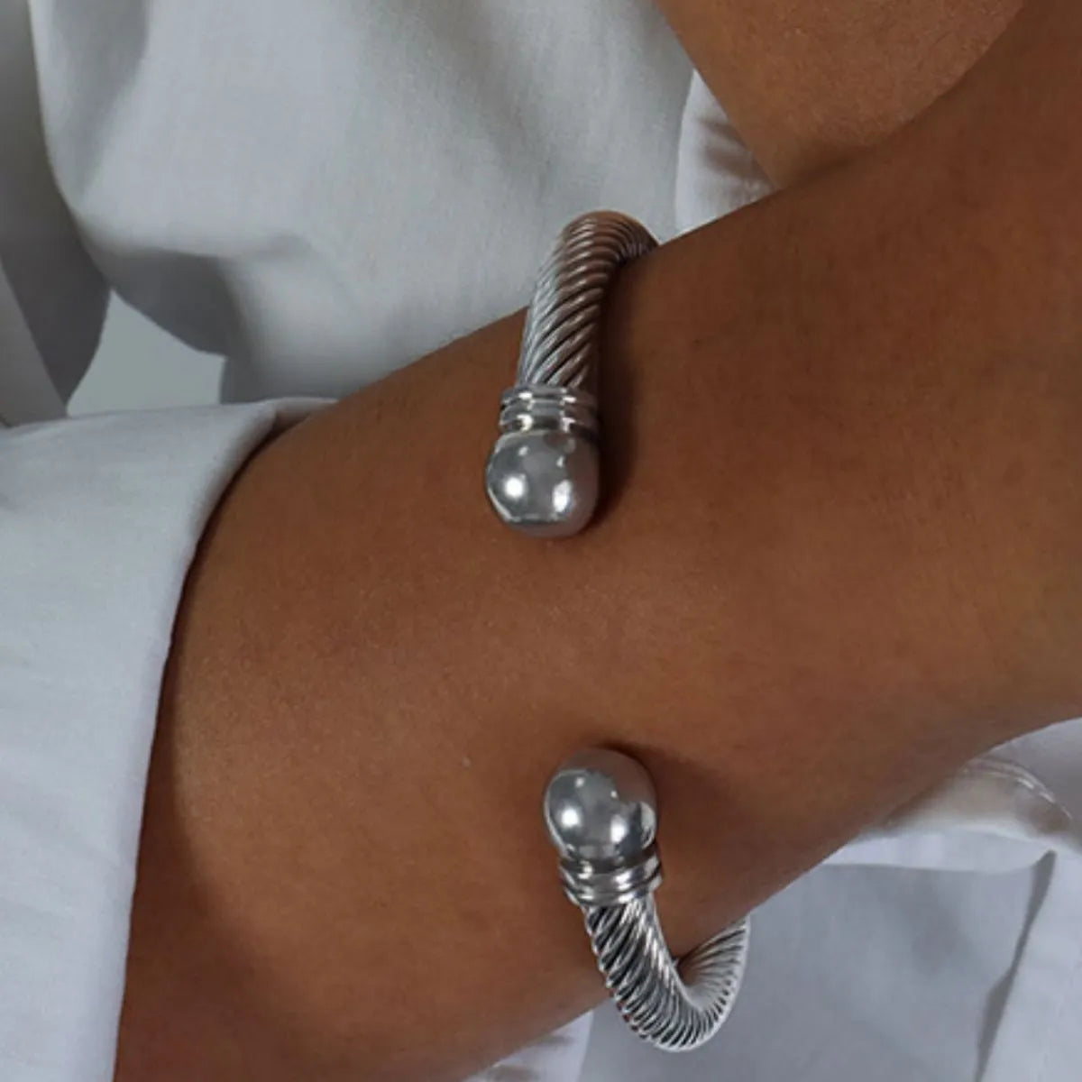 Close-up of a twisted cable cuff bracelet in 18K gold-plated stainless steel worn on wrist with white shirt sleeve