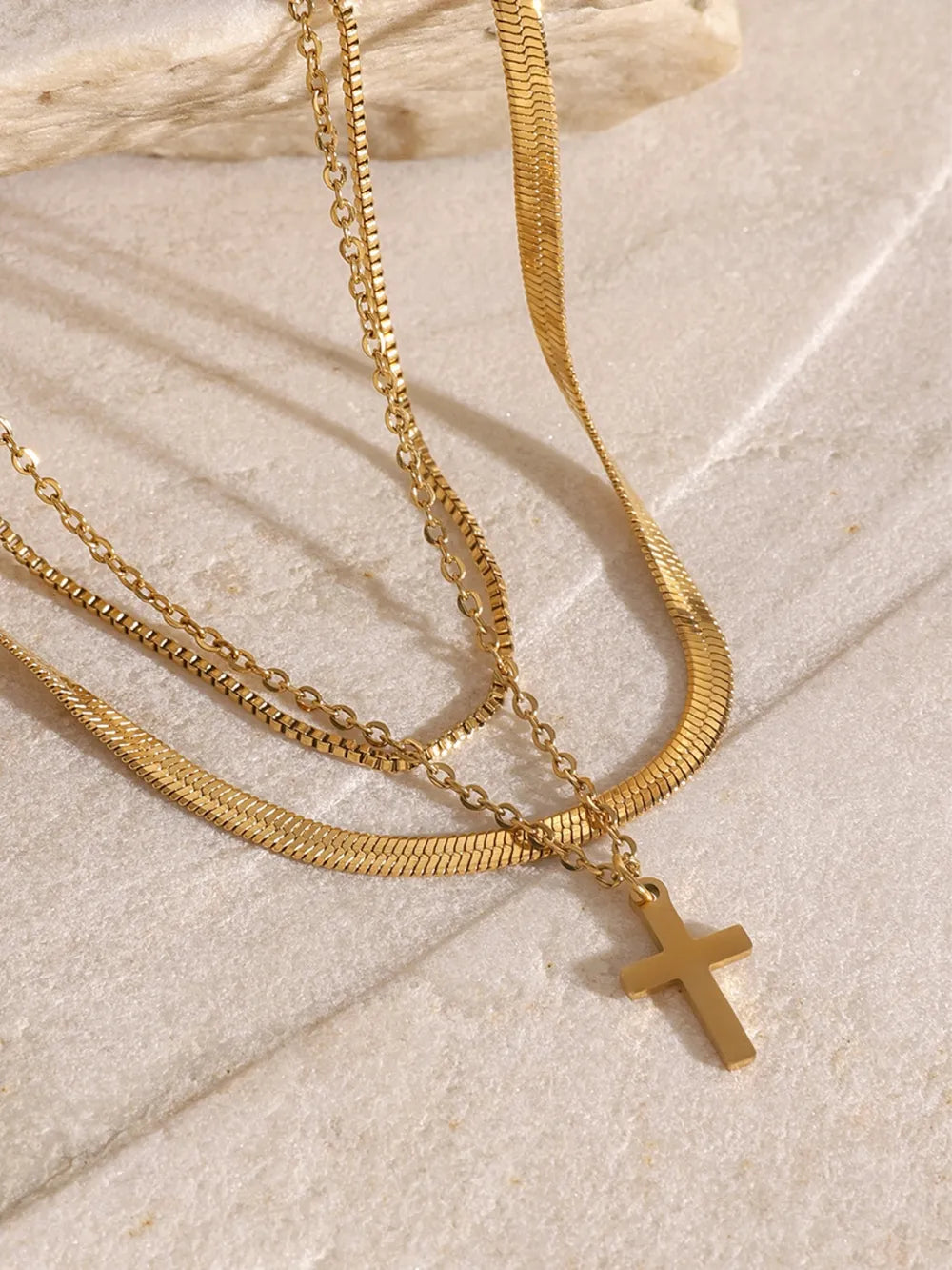 Three-layered 18K gold-plated cross necklace with varied chain styles on a neutral background.