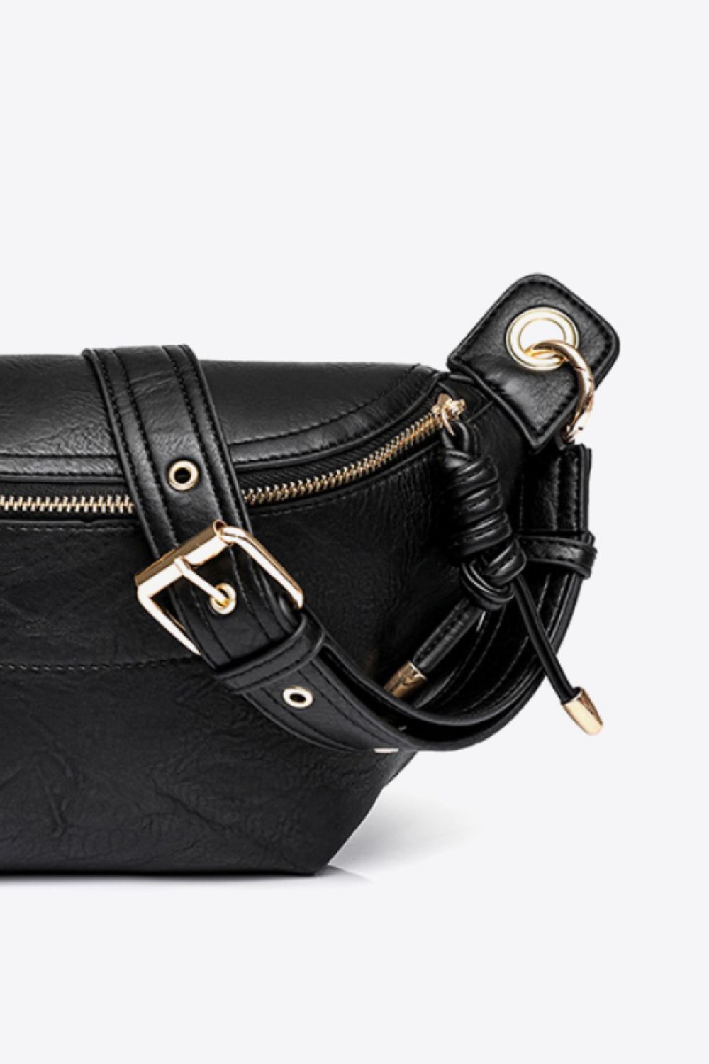 Close-up of black PU leather sling bag with gold zipper and adjustable strap detailing on white background