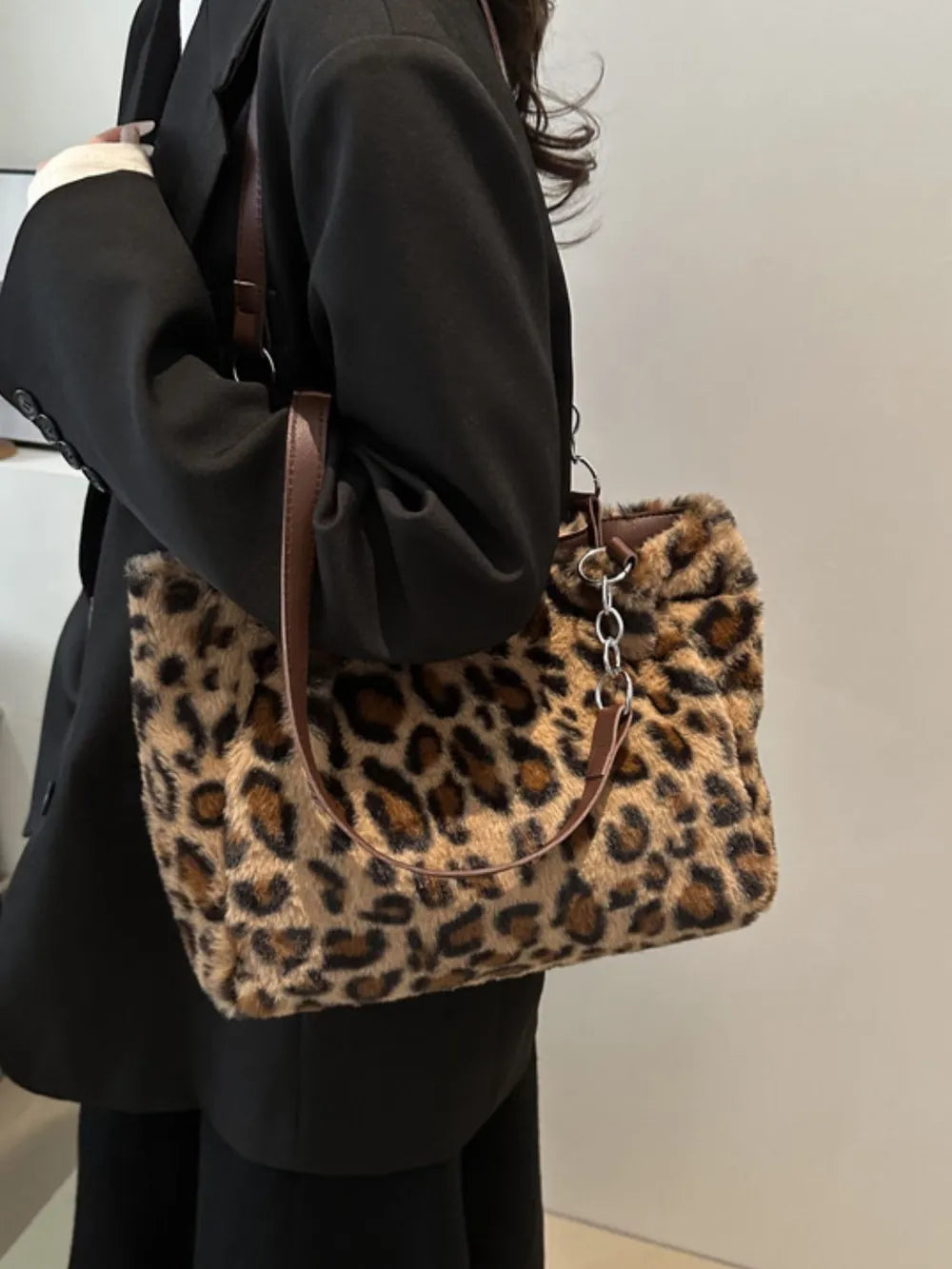 Large leopard print shoulder bag made of soft faux fur with brown adjustable strap, worn with black blazer outfit.