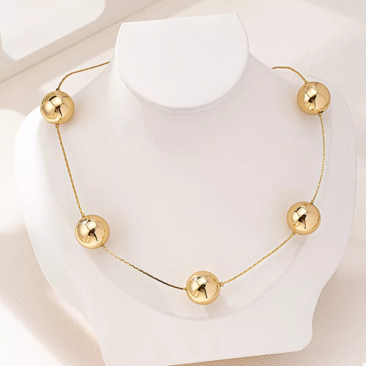 Elegant golden sphere statement necklace with five polished 18K gold-plated beads on a delicate chain displayed on a white bust.