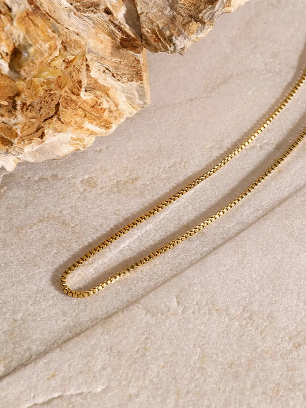 Close-up of the 18K gold-plated chain from the three-layered cross necklace on a textured stone surface.