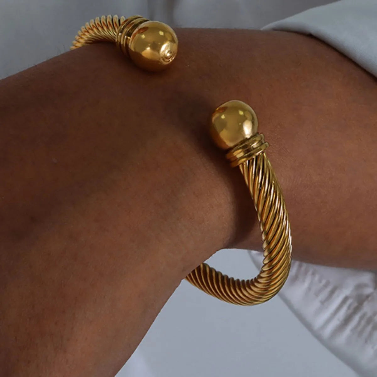 Close-up of an 18K gold-plated twisted cable cuff bracelet worn on wrist, featuring rounded ends and elegant design.