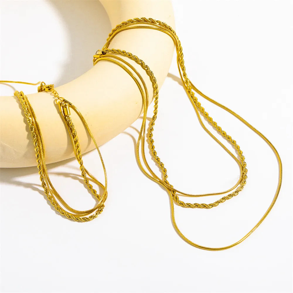 Three-layered twisted rope necklace in radiant 18K gold-coated titanium steel displayed on a beige prop.