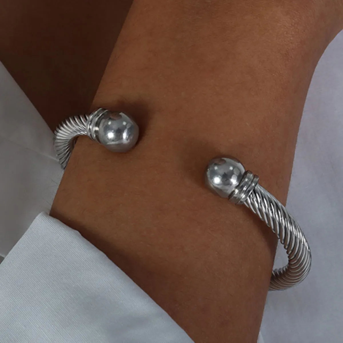 Silver twisted cable cuff bracelet worn on wrist with rounded end caps and a textured design