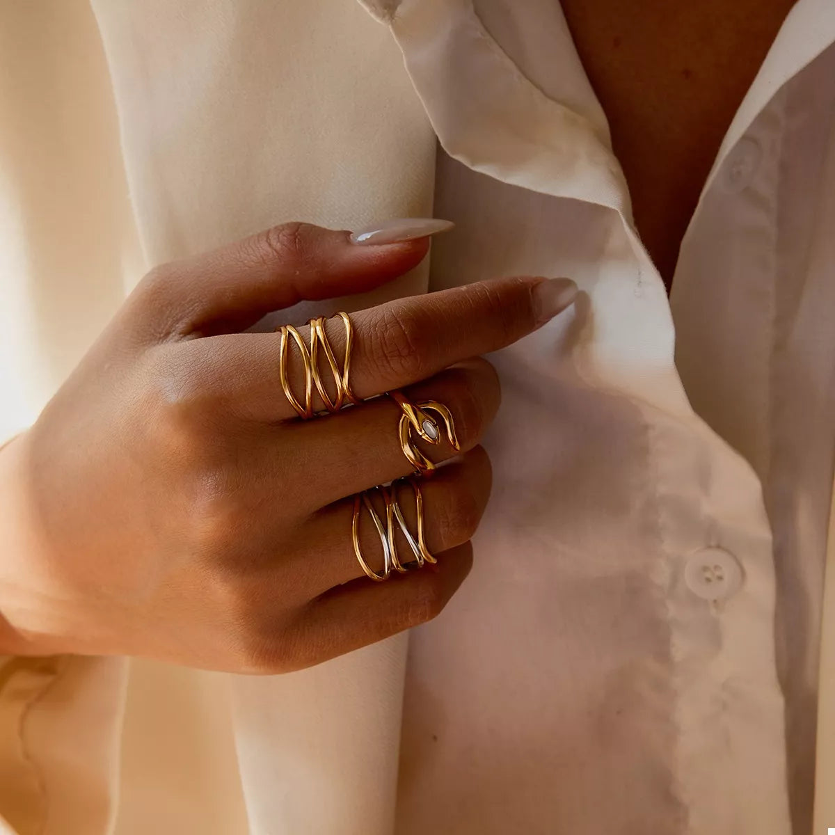 Hand wearing adjustable two-tone open rings in gold and silver plated stainless steel on fingers against white shirt background