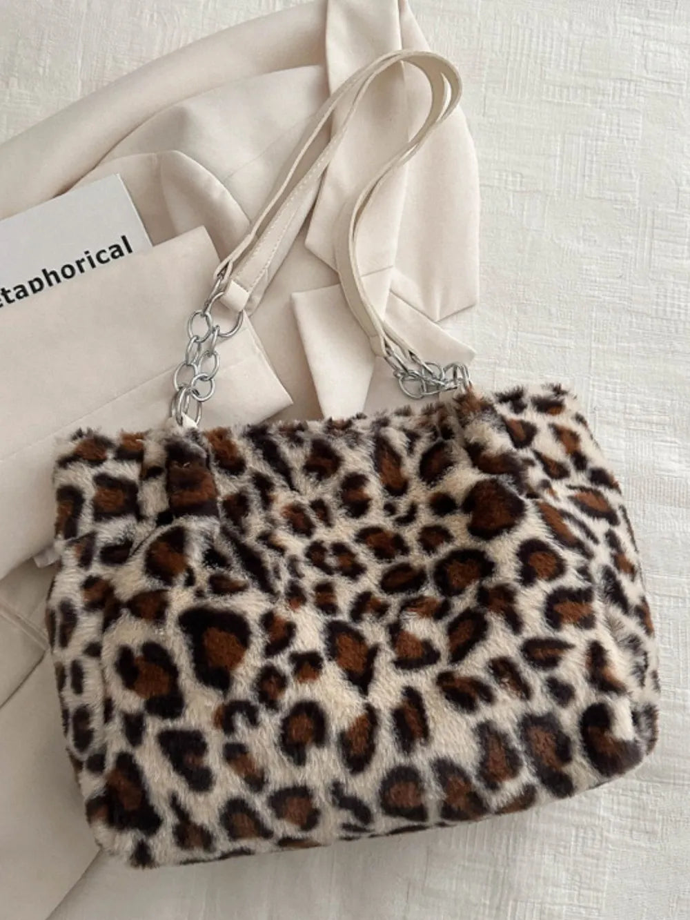 Large leopard print shoulder bag in soft faux fur with beige straps and silver chain accents on a light fabric background