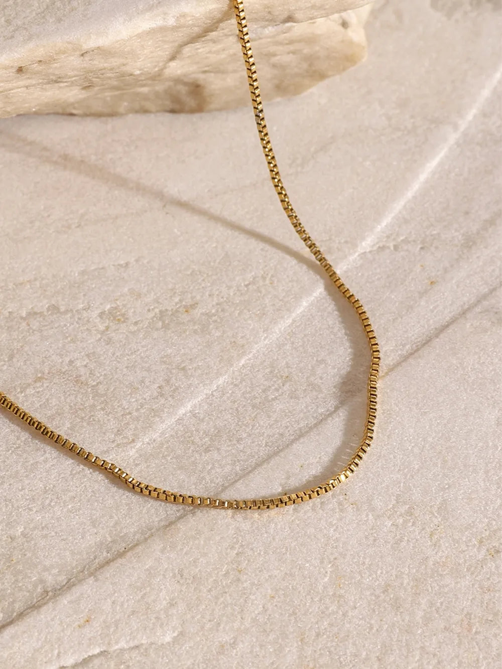 Close-up of the 18K gold-plated chain from the three-layered cross necklace on a marble surface.