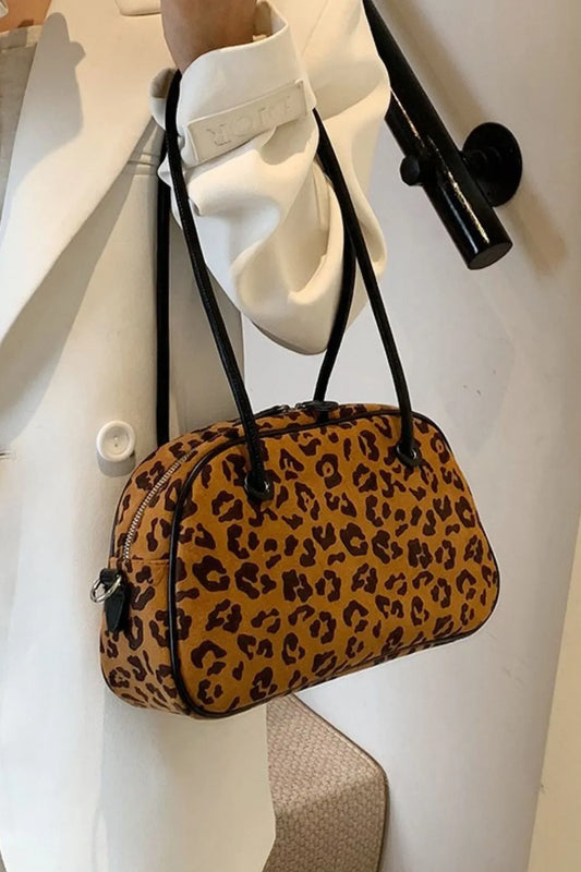 Medium leopard print suede shoulder bag with black straps, held by person wearing white coat.