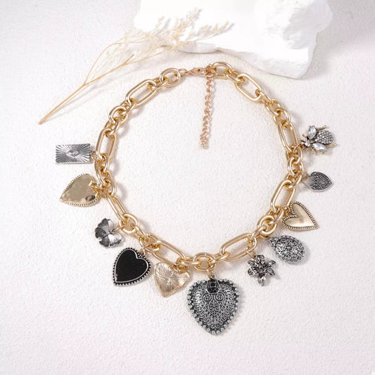 Gold chain necklace featuring multiple vintage heart and floral charms with mixed metal finishes on a white background.