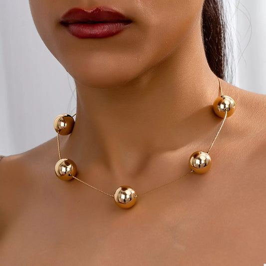 Close-up of a woman wearing an 18K gold-plated alloy necklace with five large shiny golden spheres on a delicate chain