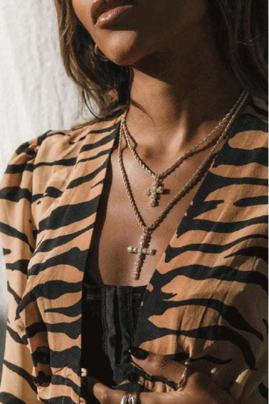 Woman wearing layered gold-plated brass necklaces with zircon cross pendants against a tiger-striped outfit