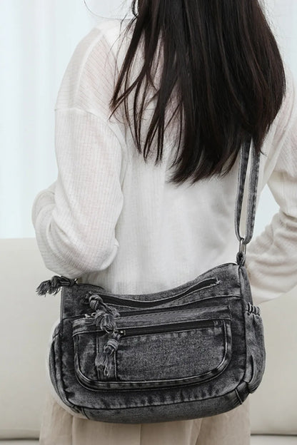 Woman wearing a medium-sized durable gray denim crossbody bag with multiple zippered compartments and adjustable strap