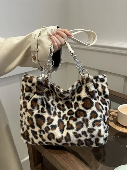 Large leopard print faux fur shoulder bag with chain and leather straps held by a person in a beige coat