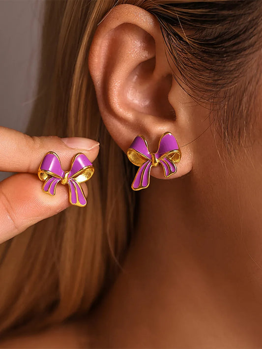 Close-up of a person wearing purple and gold bow stud earrings made from 18K gold-plated stainless steel