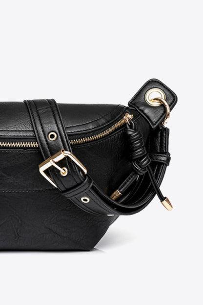Close-up of black PU leather sling bag with gold zipper and adjustable strap detailing on white background
