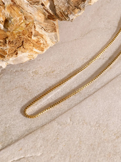Close-up of the 18K gold-plated chain from the three-layered cross necklace on a textured stone surface.