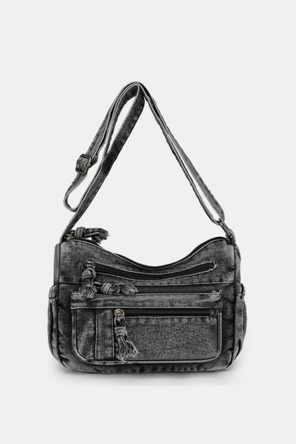 Black denim crossbody bag with multiple zippered pockets and adjustable shoulder strap against a white background