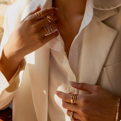 Close-up of a person wearing multiple 18K gold-plated two-tone open rings on fingers with a beige blazer and white shirt.