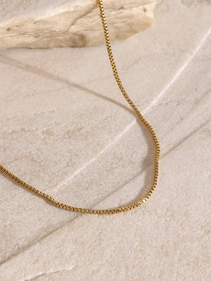 Close-up of the 18K gold-plated chain from the three-layered cross necklace on a marble surface.